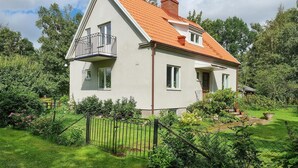 Une maison à deux étages, avec un toit recouvert de tuiles rouges, un balcon doté d’une balustrade en métal et un jardin entouré d’une clôture.