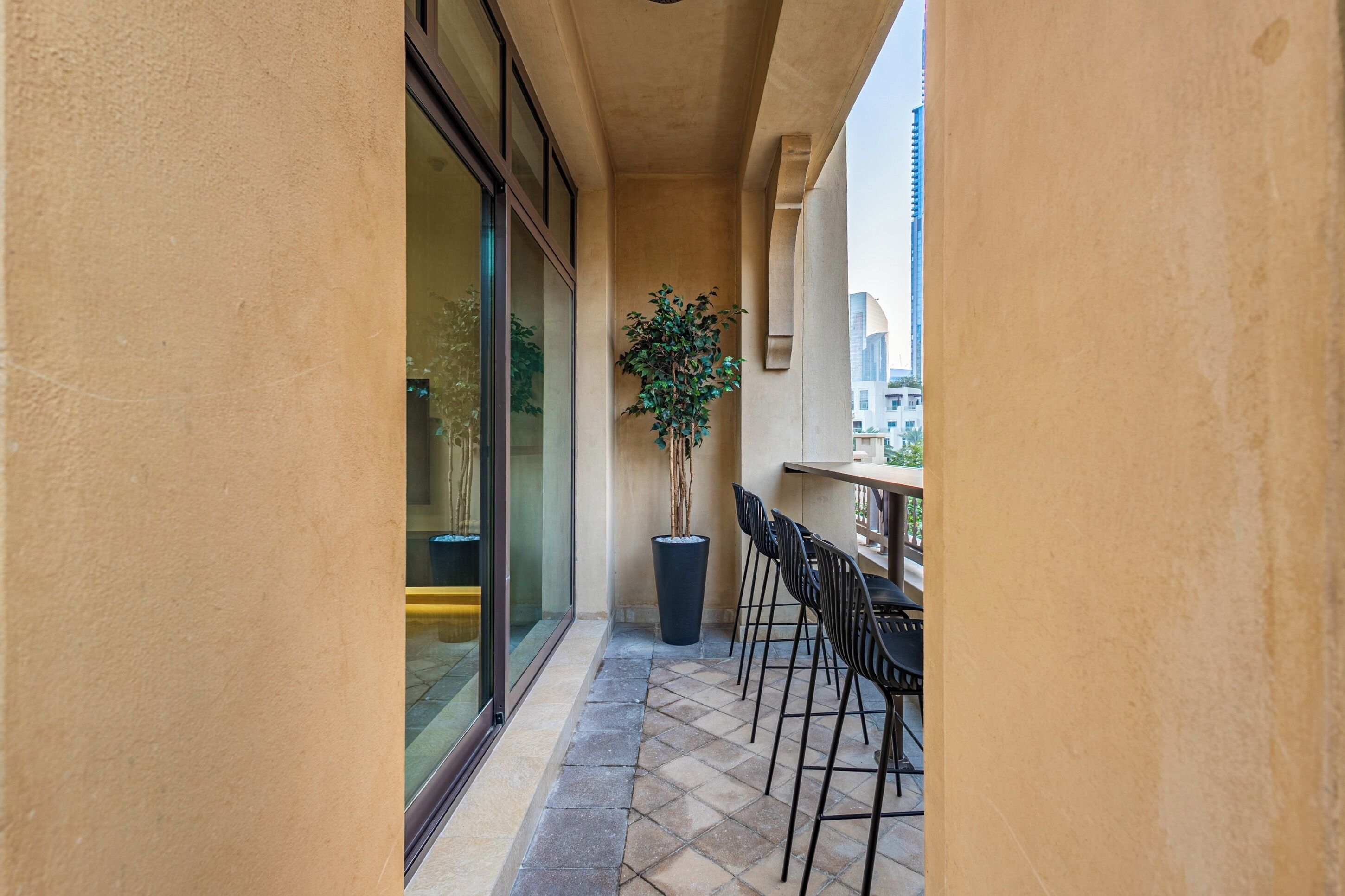 A narrow balcony with a potted plant, a table, and chairs.