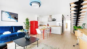 A modern living space with a blue sofa, a dining table with chairs, a kitchen area, and a staircase with a unique design. - Beautiful Apartment- 3br/10p - Montparnasse (Paris)