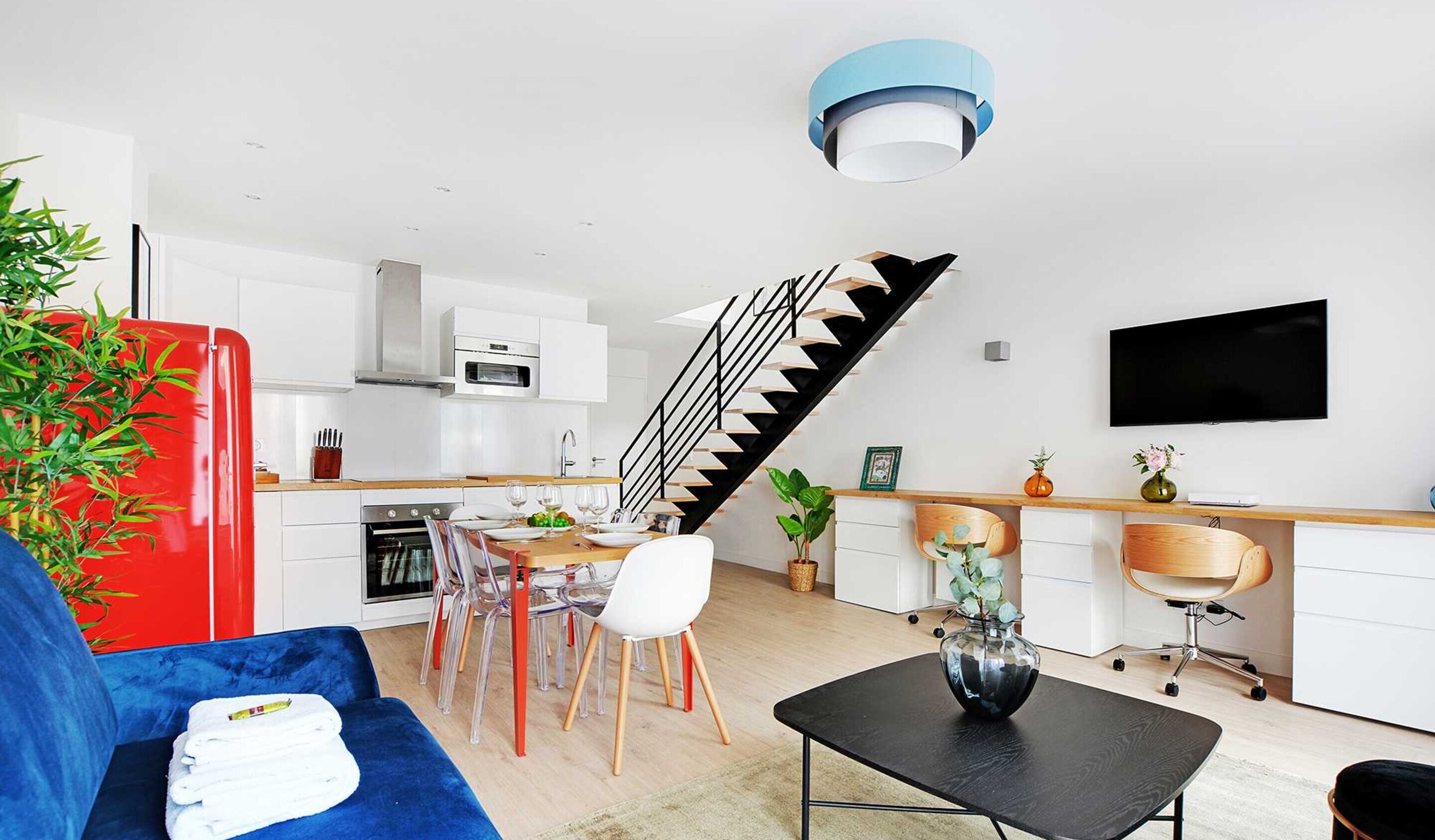 A modern kitchen with white cabinets, a black staircase, and a dining area with a blue sofa.