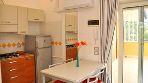 A compact kitchen with a refrigerator, stove, and a dining table with chairs. - Sunny terrace thermal baths (Bibione)