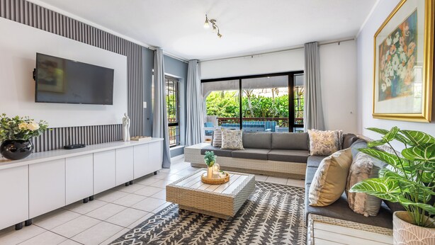A modern living room with a flat-screen TV, a sofa, a coffee table, and a potted plant. - La Pirogue, Spacious 3 Bed | Willards Beach | Pool (Dolphin Coast)