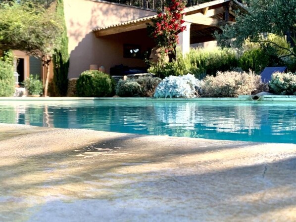 A swimming pool with clear water, surrounded by lush greenery and a building with a beige facade. - Villa infinity pool near Lourmarin (Lauris)
