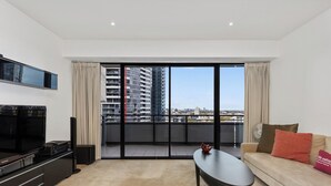 Una sala de estar moderna con un televisor de pantalla plana, un sofá, una mesa de centro y un balcón con vista a la ciudad.