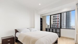 Un dormitorio moderno con una cama grande, una mesita de noche, un armario empotrado y vistas a la ciudad a través de un ventanal amplio.