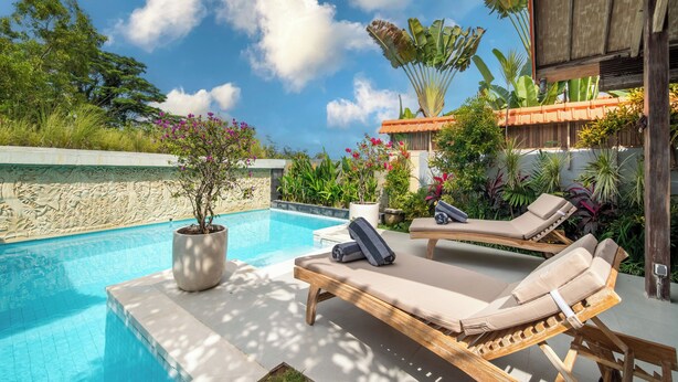 A poolside area with lounge chairs, a potted plant, and a stone wall. - Tropical Villa Senang (Ungasan)