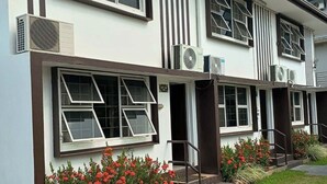 A two-story building with multiple windows, air conditioning units, and a small garden with red flowers. - Gray Inn (Nadi)