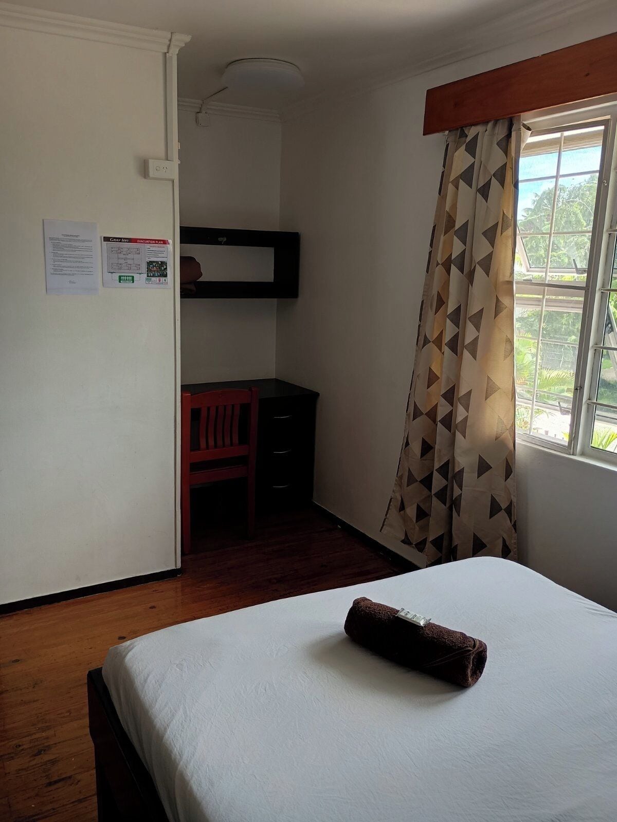 Une chambre d’hôtel avec un lit, un bureau et une chaise, une fenêtre avec des rideaux et un luminaire au plafond.