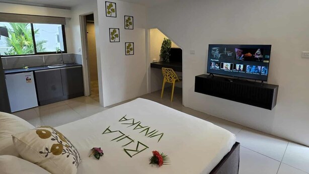A modern bedroom with a bed, a TV, and a kitchen area visible through an open door. - Gray Inn (Nadi)