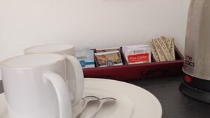 A white mug on a plate, a spoon, a coffee maker, and a tray with coffee pods and a packet of Pure Ceylon coffee. - Gray Inn (Nadi)