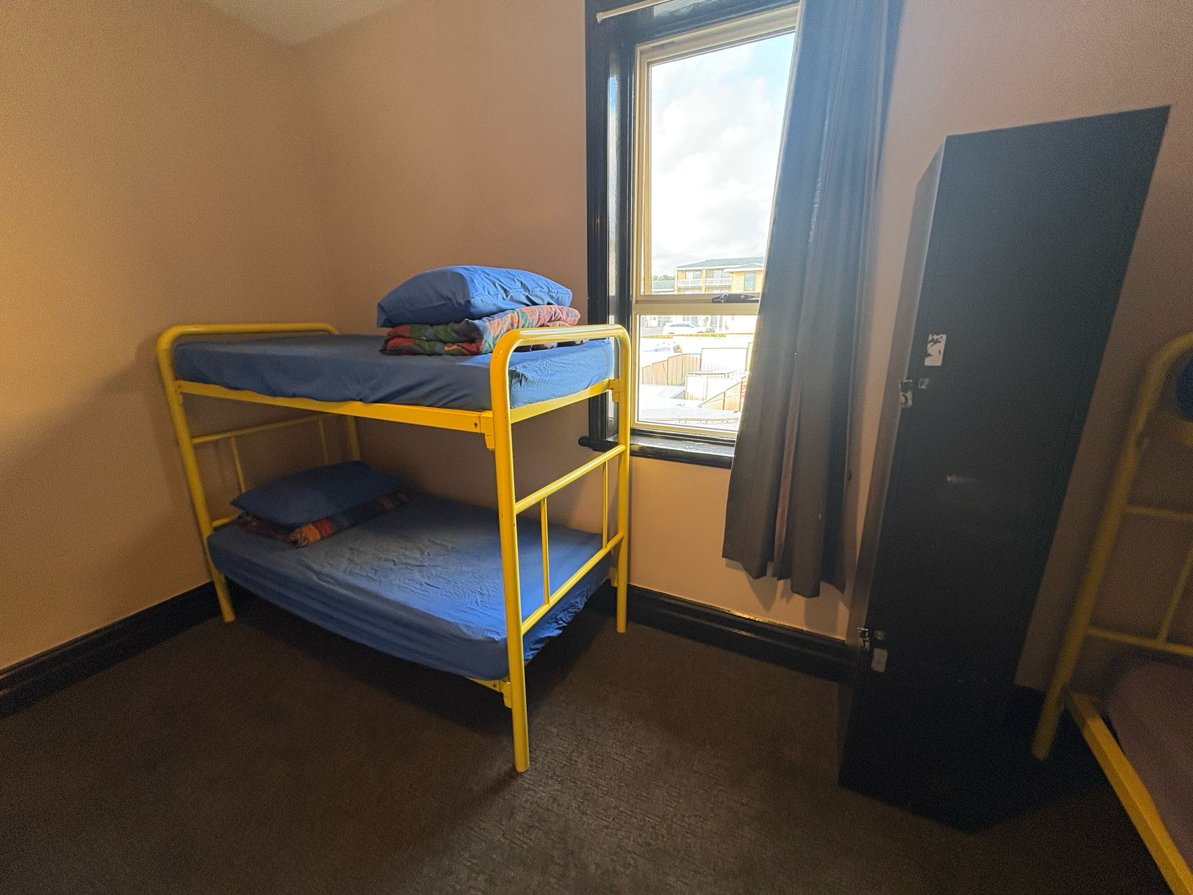 Una cama litera con ropa de cama azul en una habitación con ventana y puerta.