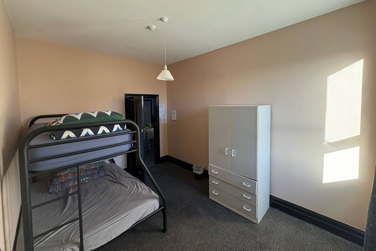 A room with bunk beds, a wardrobe, and a door leading to another room.