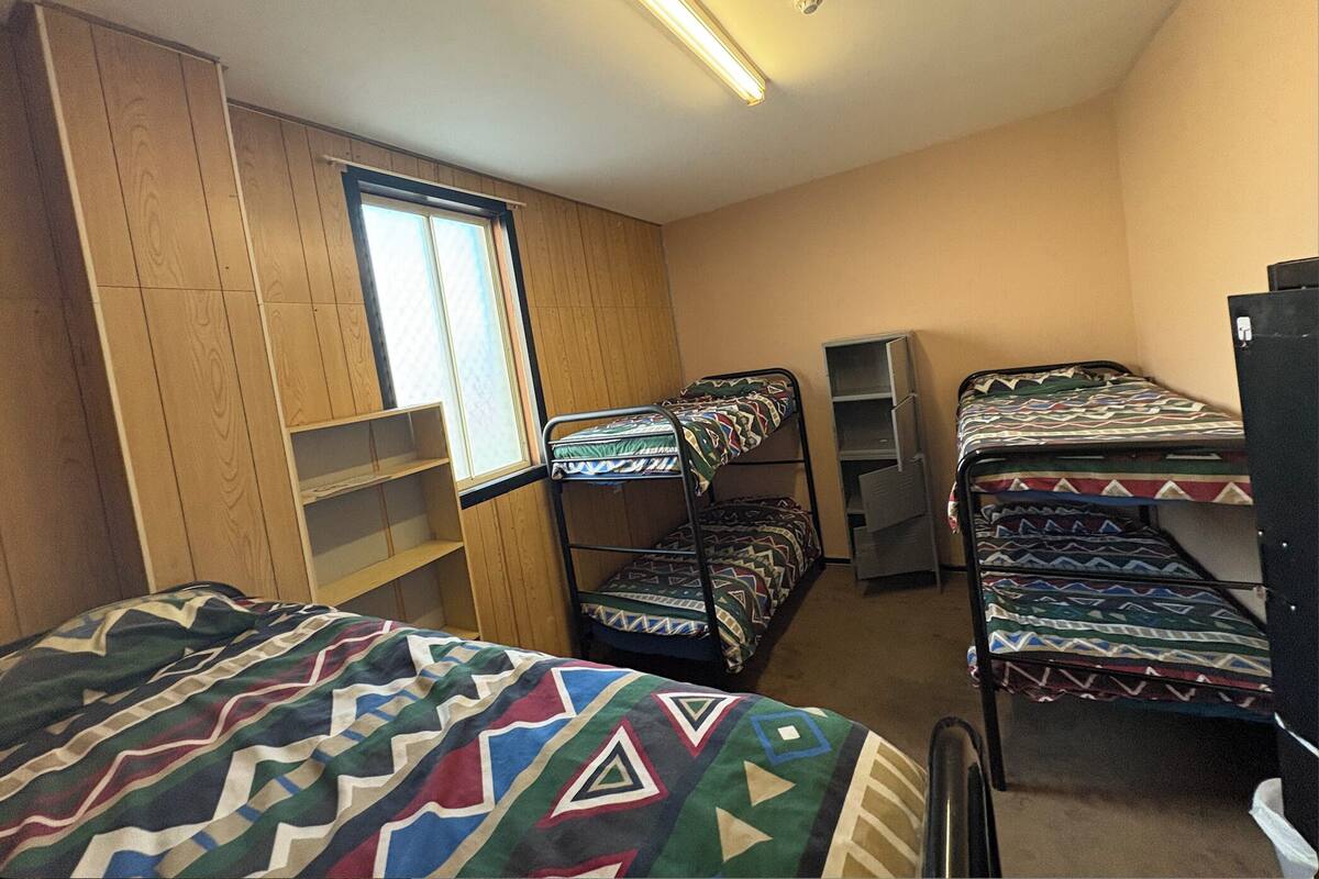 A dormitory room with bunk beds, a window, wooden paneling, and a ceiling light.