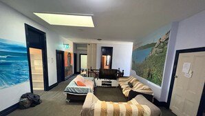 Et hotelværelse med to senge, et skrivebord og et muralmaleri af en strandscene.