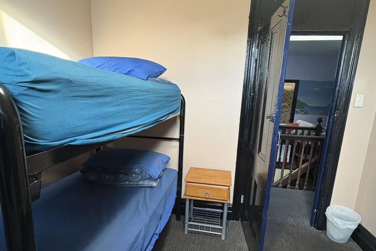 A small, compact room with bunk beds, a small wooden nightstand, and a door leading to a staircase.