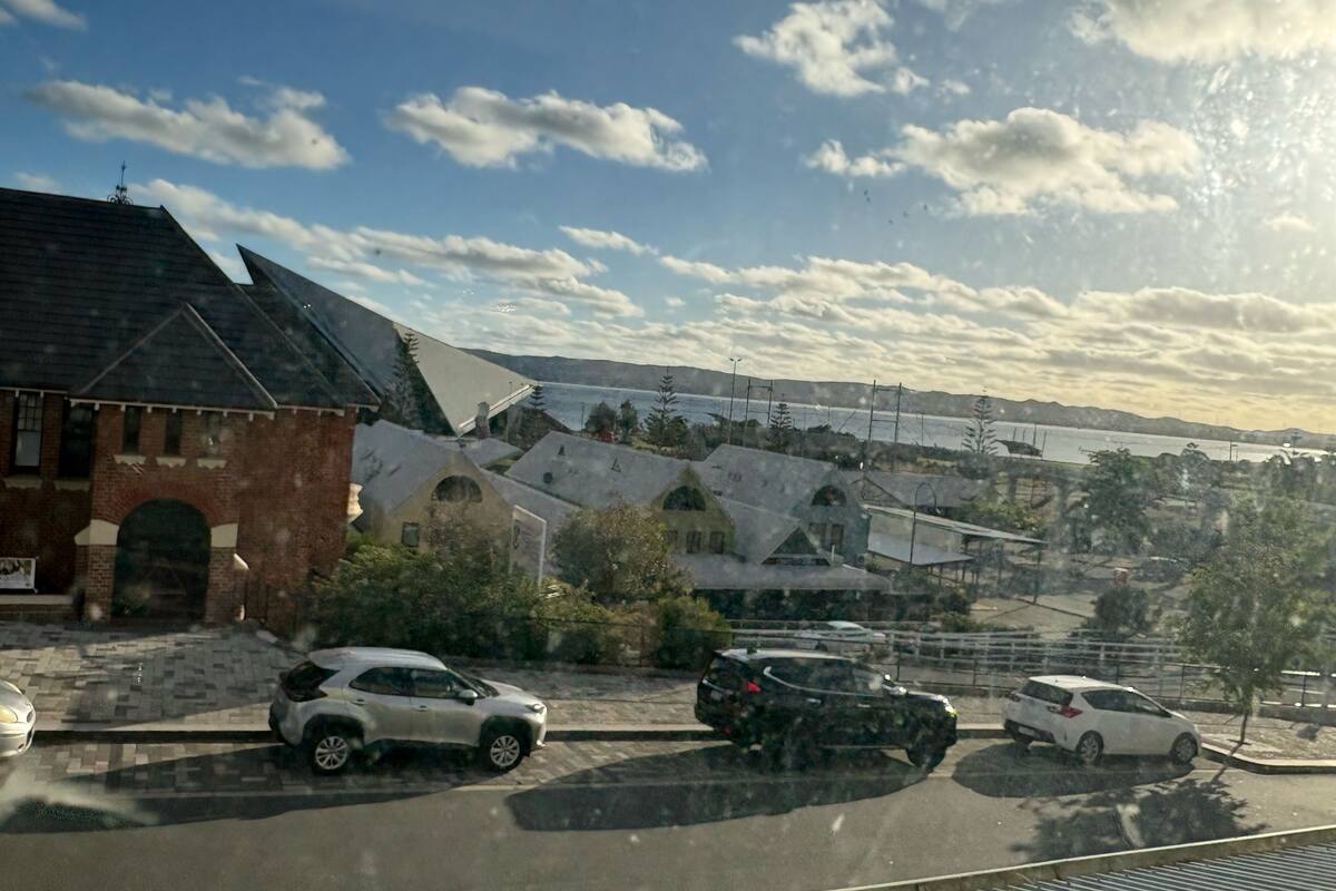 A parking area with several cars, a building with a brick facade, and a mountainous landscape in the background.