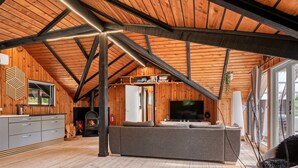 Un loft amplio con techos altos, vigas de madera a la vista, chimenea integrada, un sofá gris grande y un televisor.