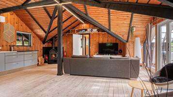 Un loft amplio con techos altos, vigas de madera a la vista, chimenea integrada, un sofá gris grande y un televisor.