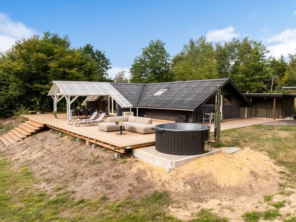 A modern outdoor living area with a hot tub, seating, and a covered patio.