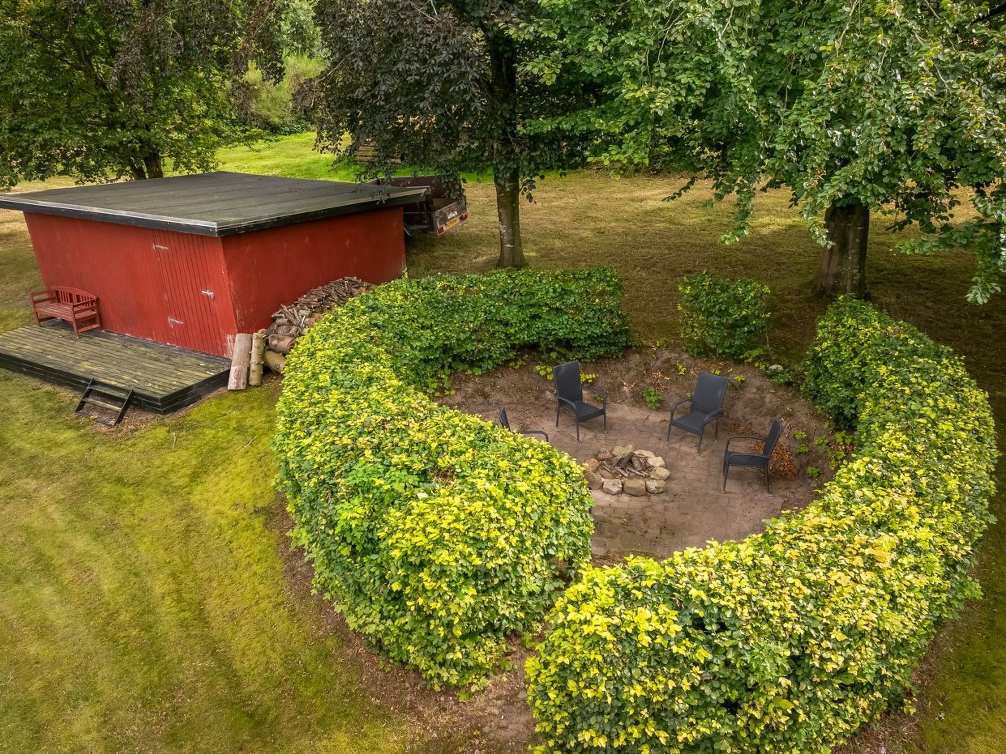 A circular garden with a fire pit and seating, surrounded by neatly trimmed bushes.