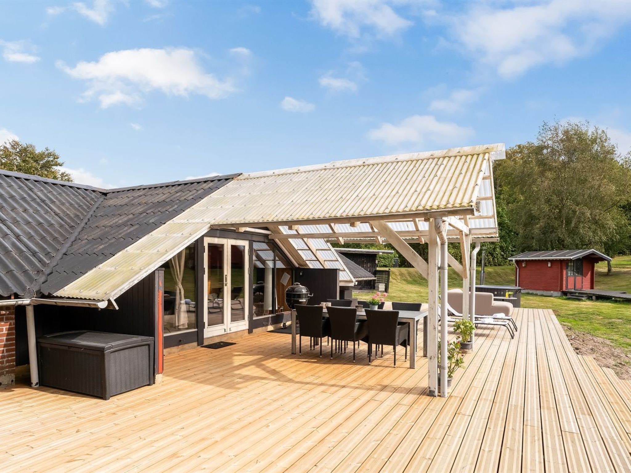 A covered outdoor patio with a wooden deck, a grill, and a seating area.