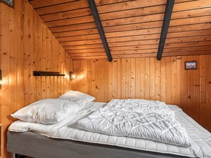 A wooden-paneled room with a bed, pillows, and a wall-mounted light fixture.