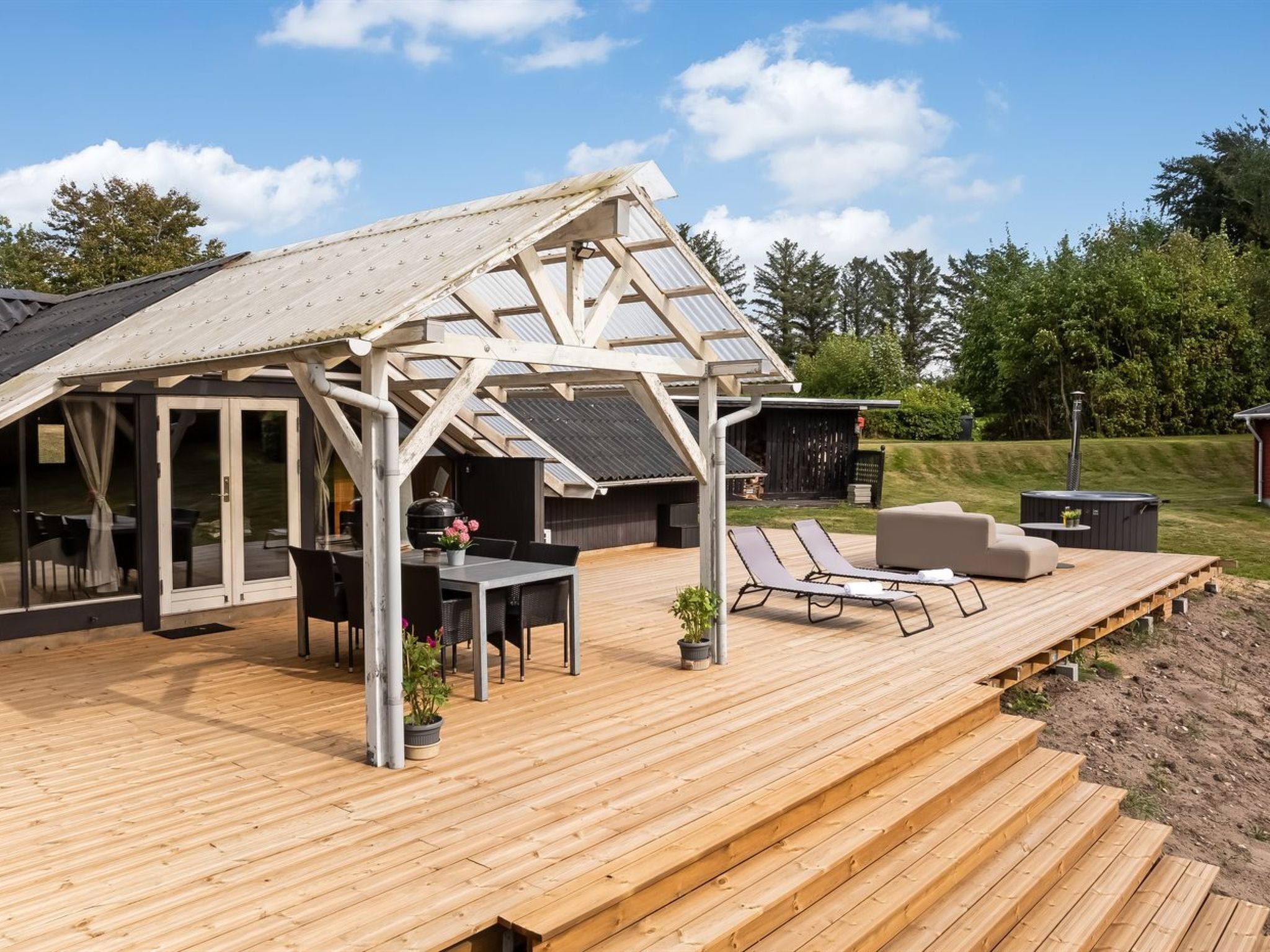 Een overdekt terras met een houten vloer, een tafel met stoelen en comfortabele fauteuils.