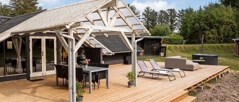 A covered outdoor area with a wooden deck, a table with chairs, and lounge chairs.