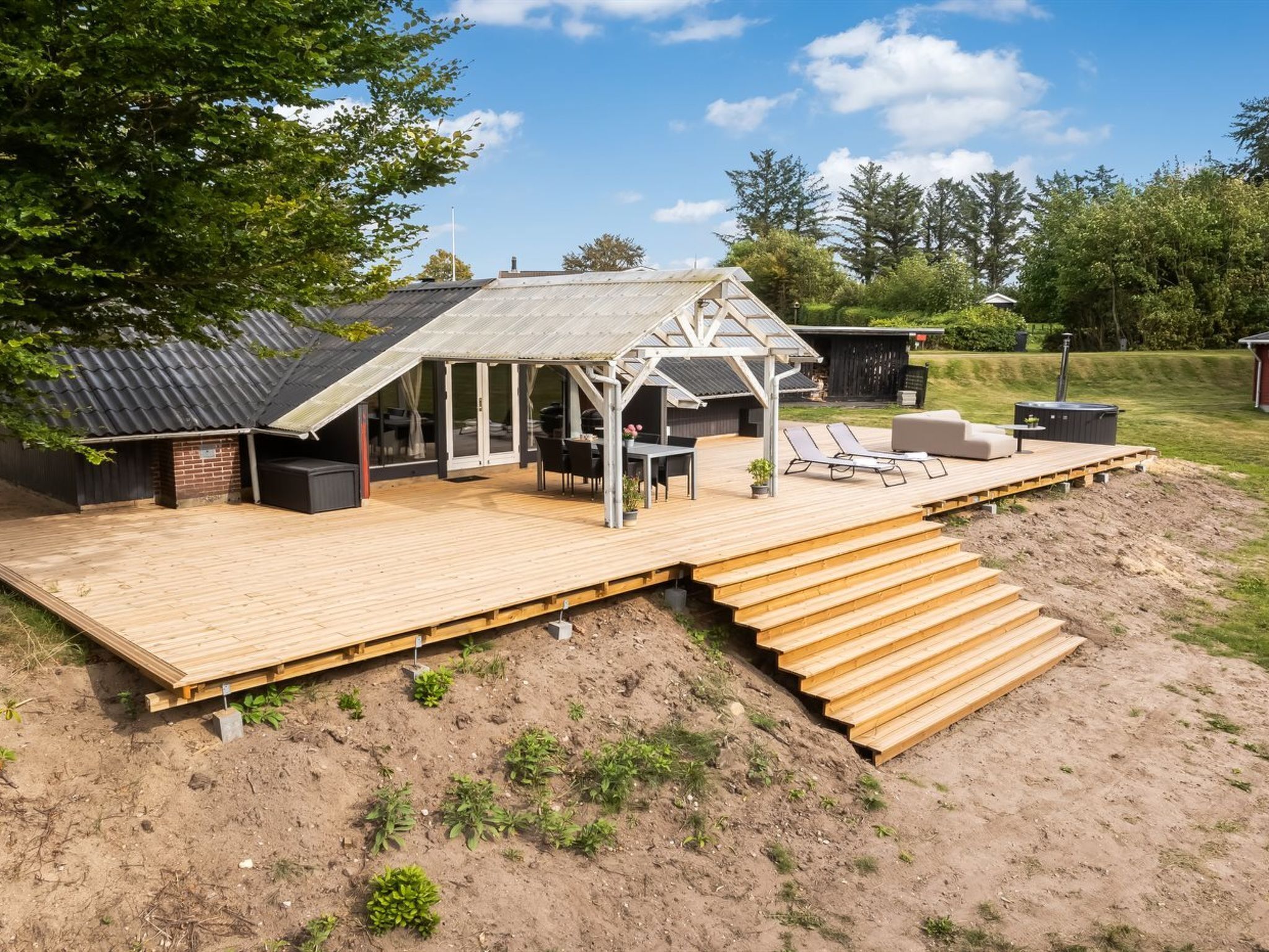 A wooden deck with a covered seating area, a barbecue grill, and a hot tub.
