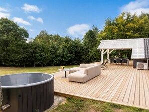 A wooden deck with outdoor furniture, a hot tub, and a covered area with a table and chairs.