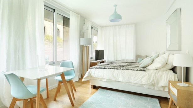 Une chambre à coucher avec un lit, une table de chevet, une lampe et une fenêtre avec des rideaux.