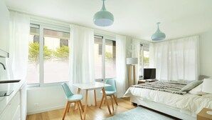 Une chambre moderne comprenant un lit, un bureau, deux chaises, un téléviseur et une fenêtre avec des rideaux.