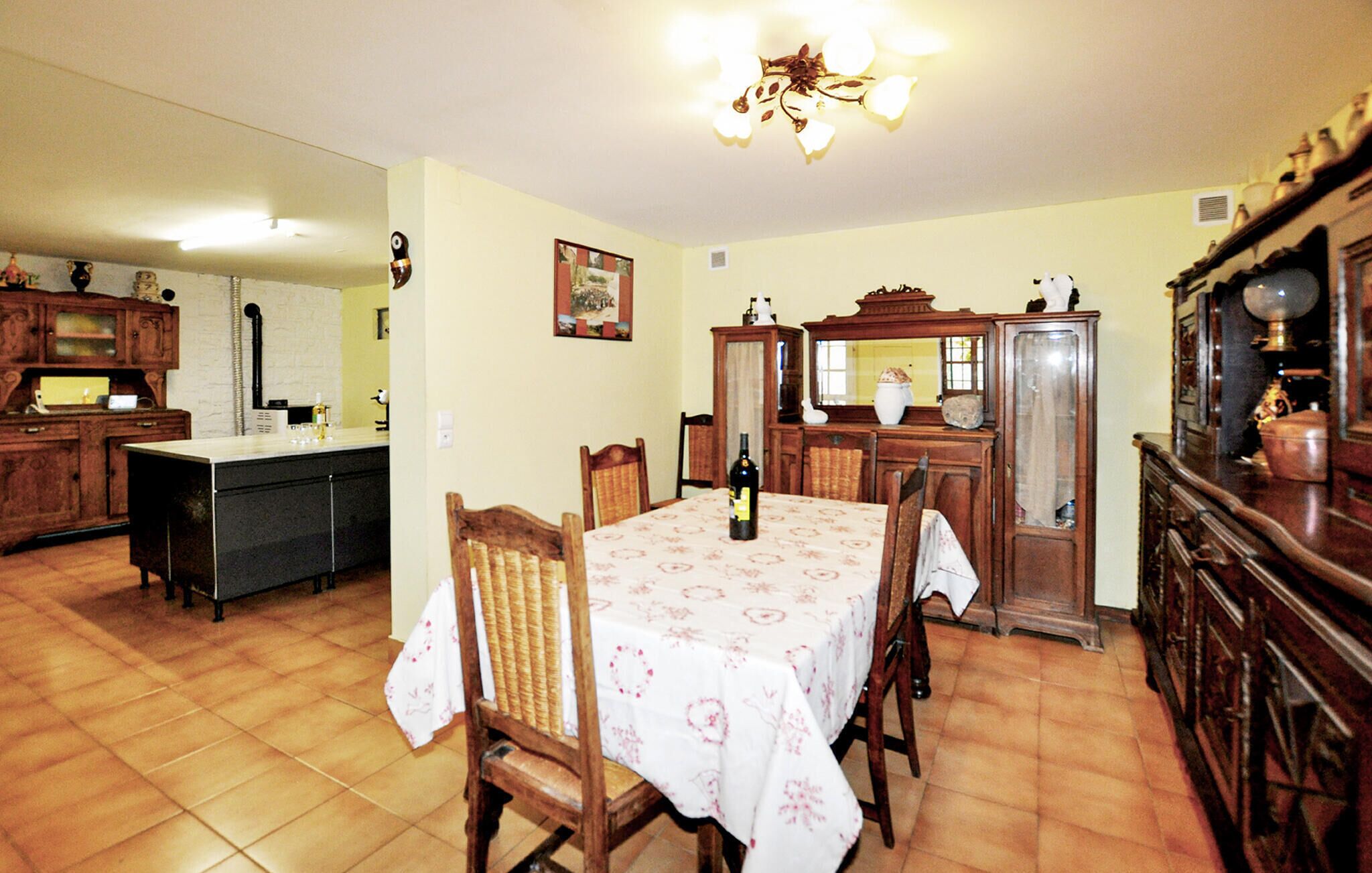 A dining area with a table set for four, surrounded by wooden chairs. A bottle of wine is on the table.