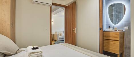 A hotel room with a bed, a wooden wardrobe, a bathroom with a marble vanity, and an air conditioning unit.