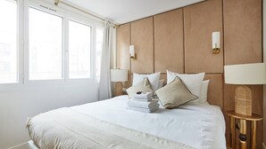 A neatly arranged hotel room with a large bed, two bedside tables with lamps, and a view of the outside through large windows. - Apartment in the Center of Paris (Paris)