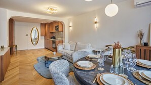 A modern dining area with a round table set for six, surrounded by upholstered chairs. A kitchen area with wooden cabinets and a built-in oven is visible in the background. - Apartment in the Center of Paris (Paris)