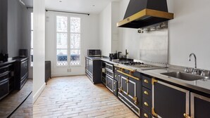 A modern kitchen with a large island, stainless steel appliances, and a black range hood. - Sublime 3 Bedroom Flat Palais Royal Bourse (Paris)