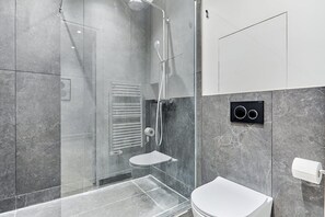 A modern bathroom with a glass-enclosed shower, a toilet, and a wall-mounted toilet paper holder. - Sublime 3 Bedroom Flat Palais Royal Bourse (Paris)