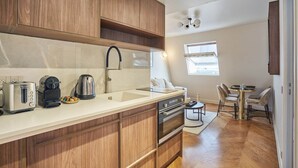 A modern kitchen with wooden cabinets, a built-in oven, and a sink. There is a dining area with a table and chairs. - New Apartment Center of Paris/le Marais (Paris)
