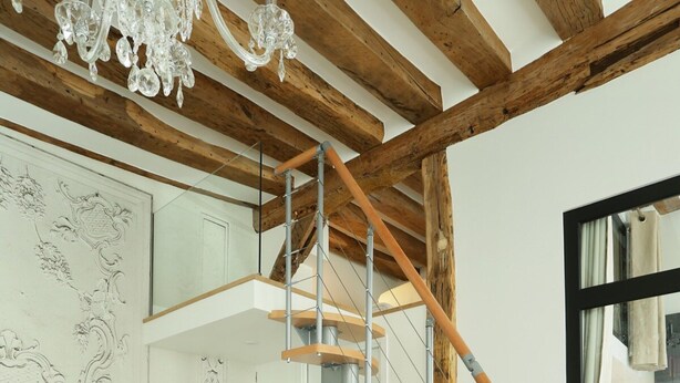 Uma sala moderna com escada de madeira, sofá cinza e lustre.