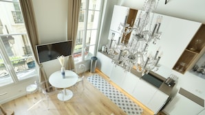 A modern kitchen with a chandelier, white cabinets, and a dining area with a table and chairs. - Superb Apartment Le Marais Center of Paris (Paris)