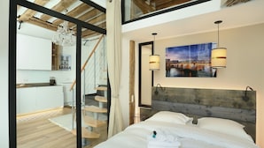A modern bedroom with a wooden headboard, a large bed with white linens, two bedside lamps, and a cityscape painting on the wall. - Superb Apartment Le Marais Center of Paris (Paris)