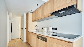 A modern kitchen with wooden cabinets, a built-in dishwasher, a black induction cooktop, and a coffee maker. - New Flat Terrace Centre de Paris Bourse (Paris)