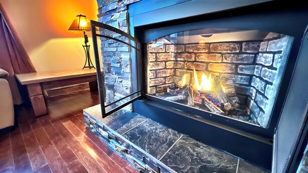 A stone fireplace with a glass door, a bench, and a lamp in a room with wooden flooring.