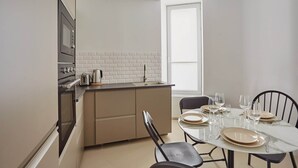 Moderni keittiö, jossa on valkoisesta tiilestä tehty seinäpaneeli, sisäänrakennettu uuni ja ruokailutila marmoripöydällä, johon on katettu neljälle.