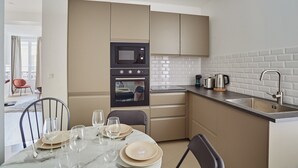 A modern kitchen with a built-in microwave and oven, a sink, and a dining area with a table set for four. - Modern Apartment Matignon Champs Elysees (Paris)