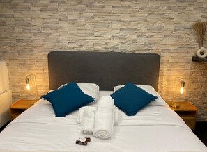 A neatly made bed with white linens and blue pillows, two bedside lamps, and a stone wall backdrop. - Charming Studio District Le Marais Center of Paris (Paris)