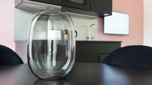 Un jarrón de vidrio transparente sobre una mesa en una cocina moderna con armarios oscuros y una pared rosa.