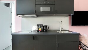 Cocina compacta con microondas, tostadora y cafetera sobre la encimera, un fregadero y un televisor montado en la pared.