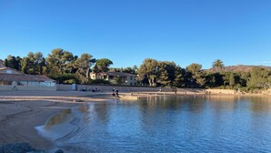 Una playa con un lago tranquilo, una orilla arenosa y edificios al fondo.